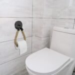 Portarotolo in corda con supporto a muro rotondo nero su una parete piastrellata del bagno accanto al WC