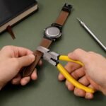 Mani che usano la pinza fora cinghie con manici gialli su un cinturino in pelle di un orologio a una scrivania