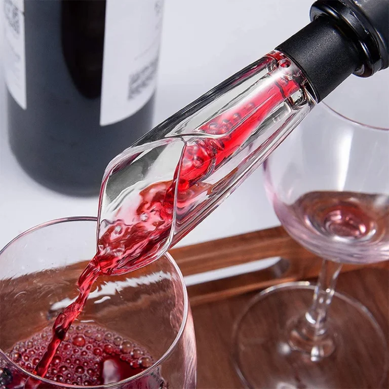 Beccuccio aeratore che versa vino rosso in un bicchiere su un vassoio di legno