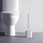 Scopino in silicone bianco nel suo supporto sul pavimento del bagno accanto al WC