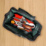 Borsa portattrezzi verde aperta con attrezzi da giardino all'interno su un pavimento in legno